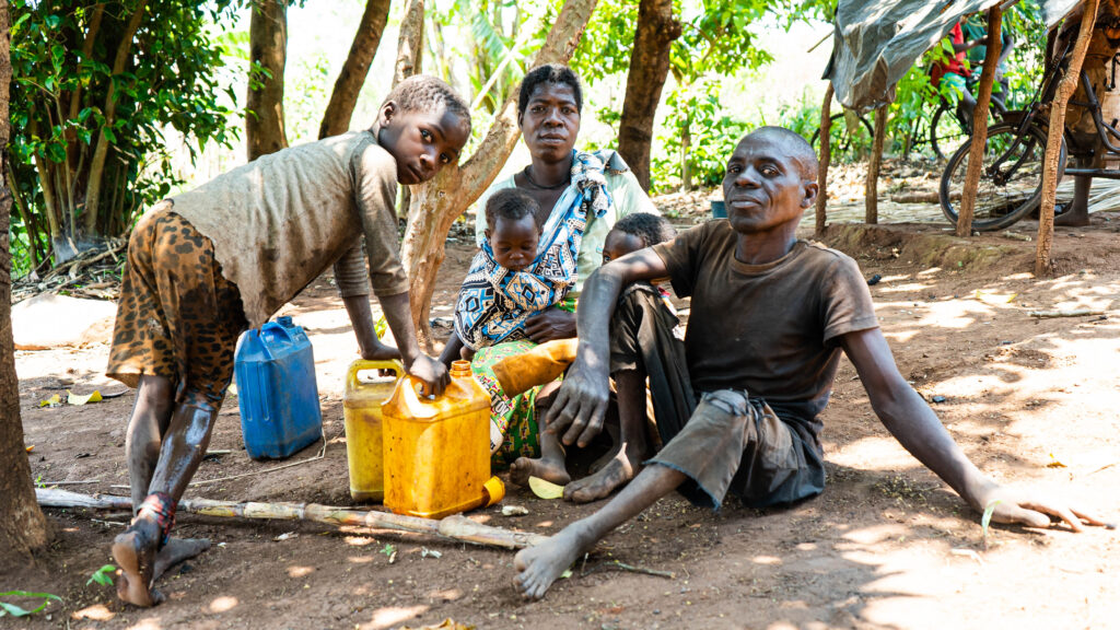 A man, a woman and three children sit together under a tree with yellow jerry cans and a hoe.
