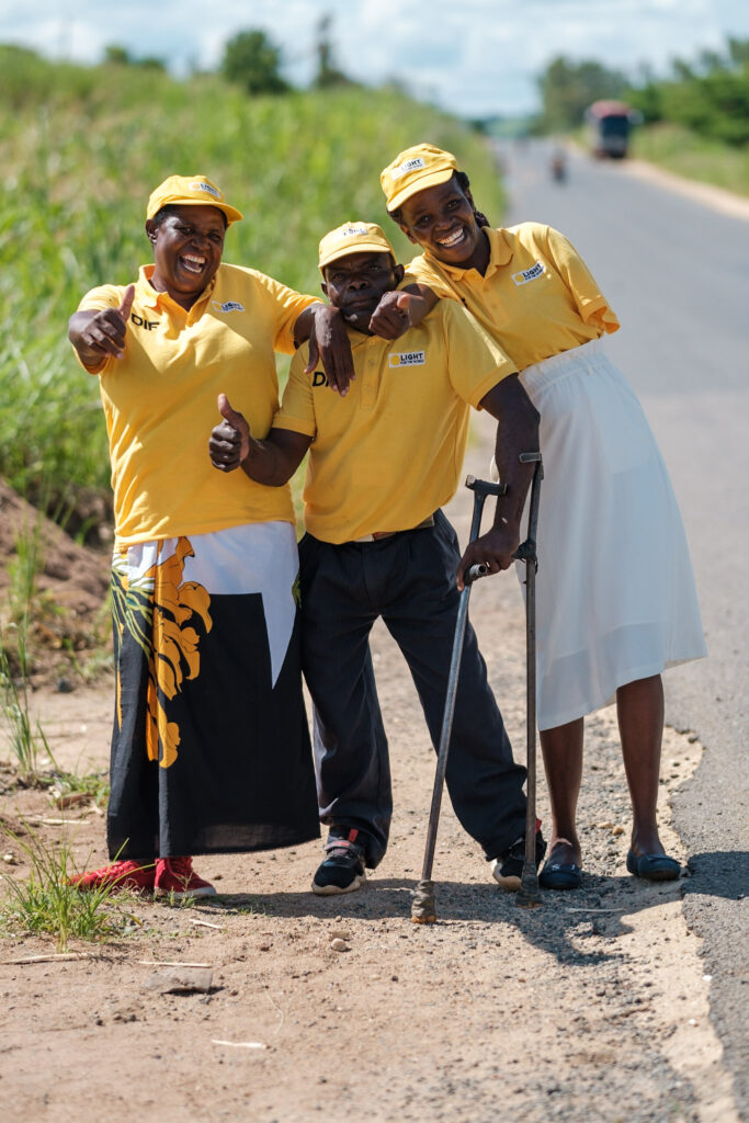 Two women with physical impairment and one man using a crutch stand next to afield posing and smiling. THey are all wearing matching yellow shirts reading DIF.