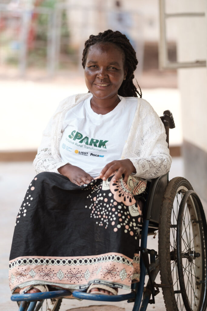 A woman in a wheelchair smiling dressed in a shirt that says SPARK.